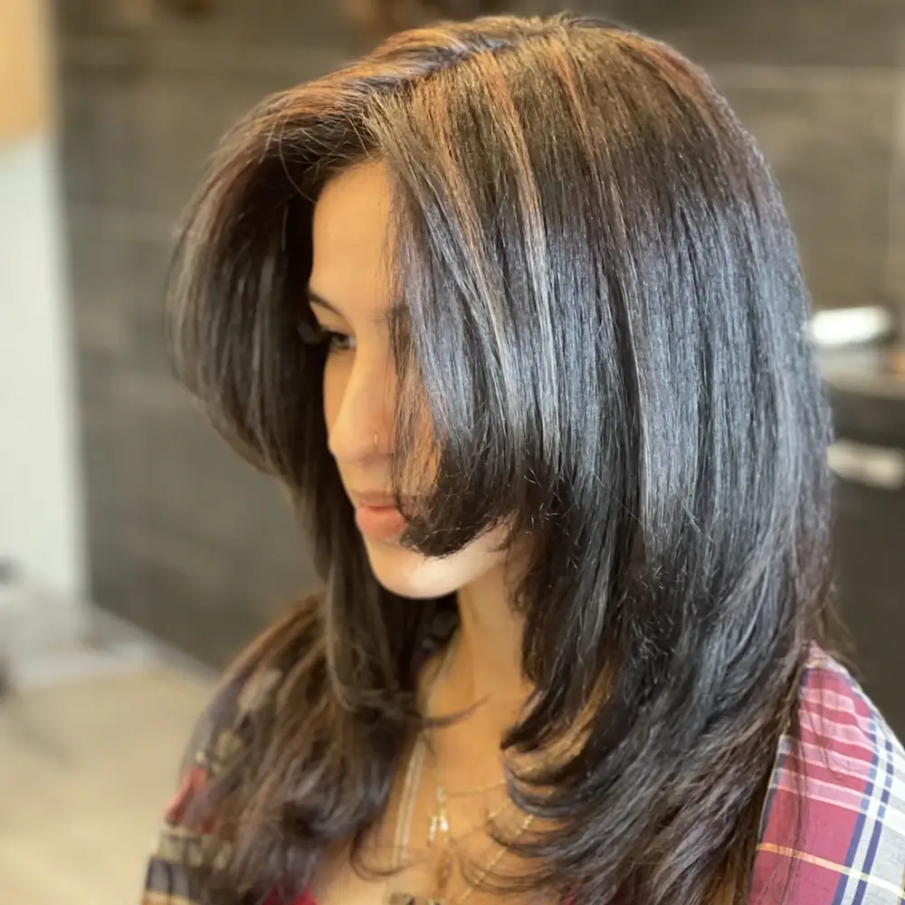 Women's medium-length layered haircut in dark brown color with a blowout and light brown highlights in Queens, NY from Larisa's Salon